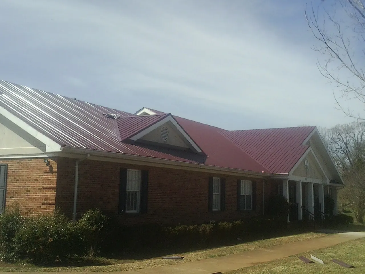 Red metal roof with gabled entries on a long brick building, from a Hail Damage Roof Repair job in Wanatah