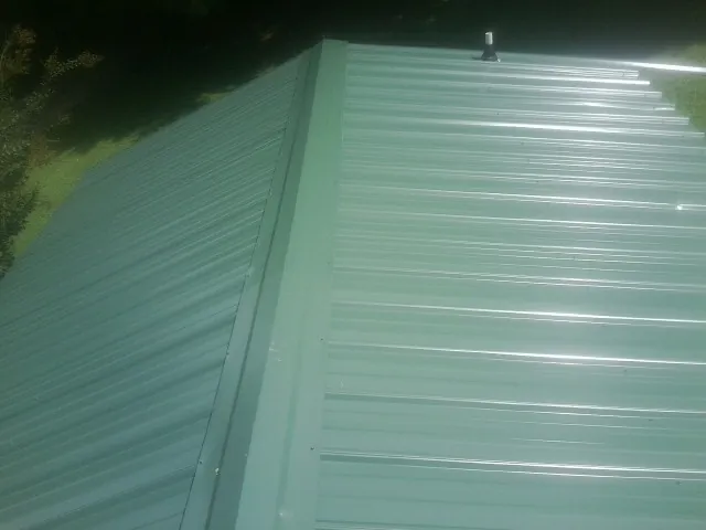 New green metal panels meeting at the ridge of a roof — Flat Roof Repair work by our crew in Wanatah