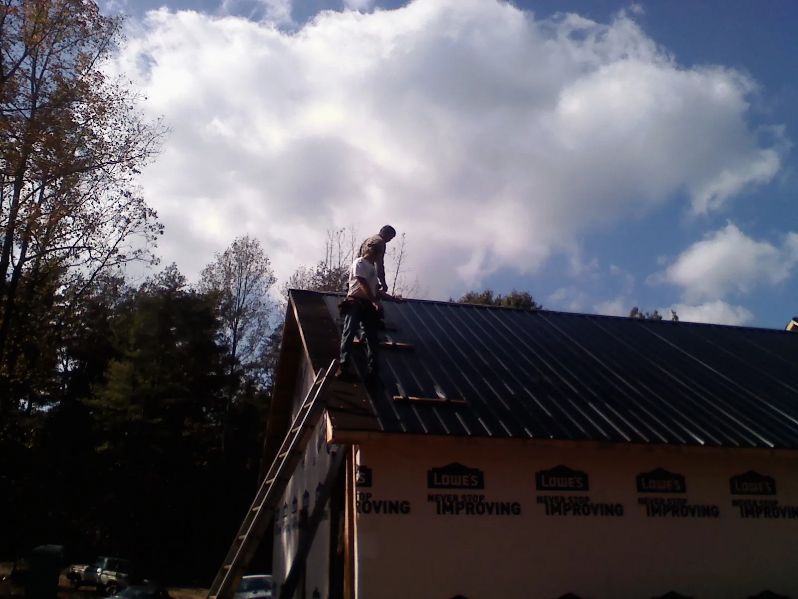 Roofer fastening dark metal panels high against a cloudy sky, from a Roof Inspection job in Wanatah