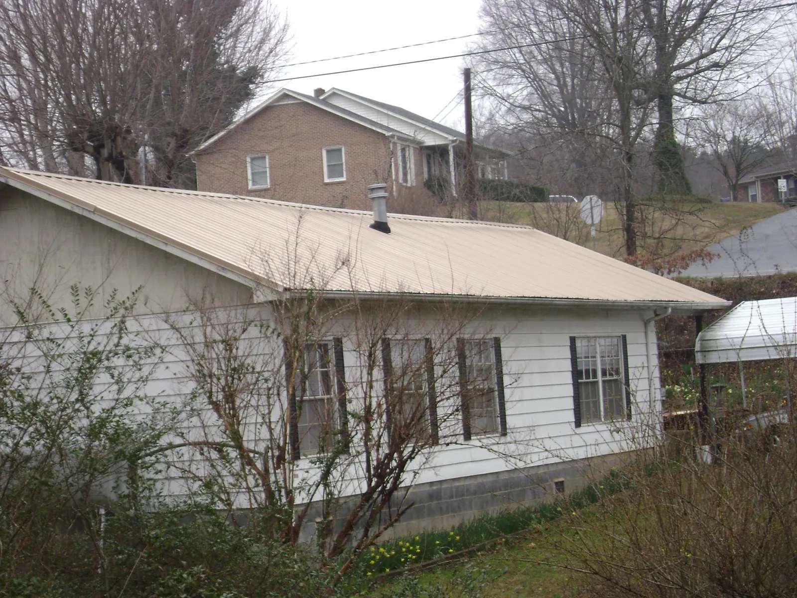 Tan metal roof on a white sided house set into a hillside — Commercial Roofing by Roofing Brothers in Wanatah